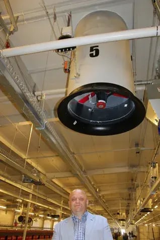 Homme debout sous un ventilateur industriel monté au plafond portant le numéro 5 dans une grande installation avicole