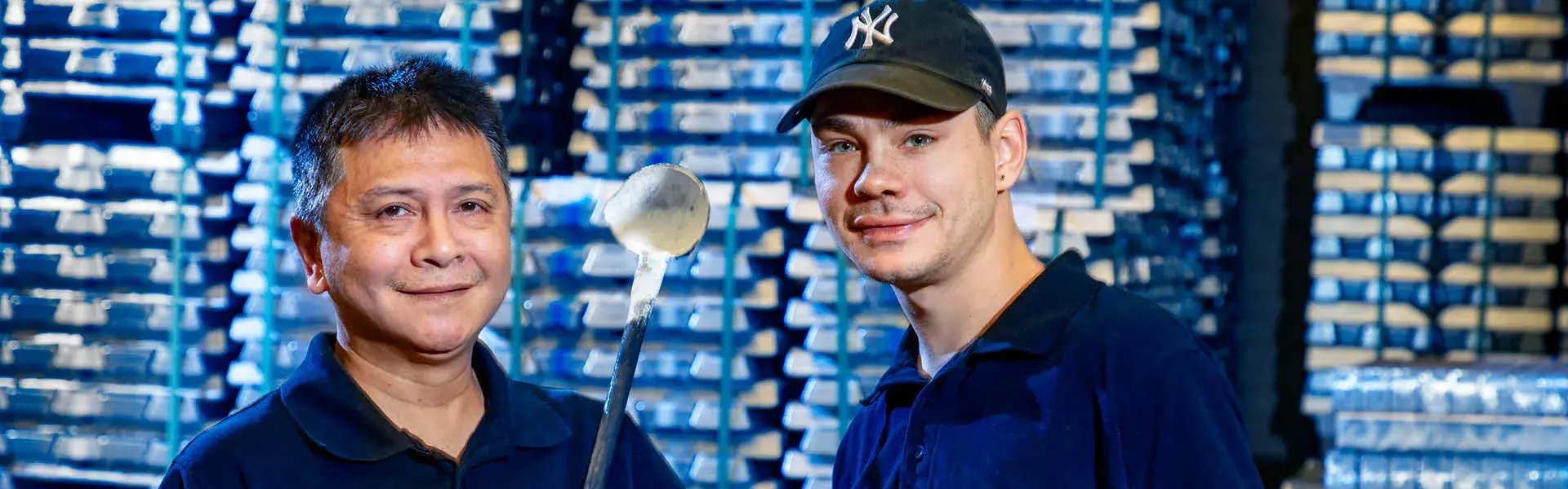 Two employees working in gravity die casting with metal molds standing in front of metal stacks