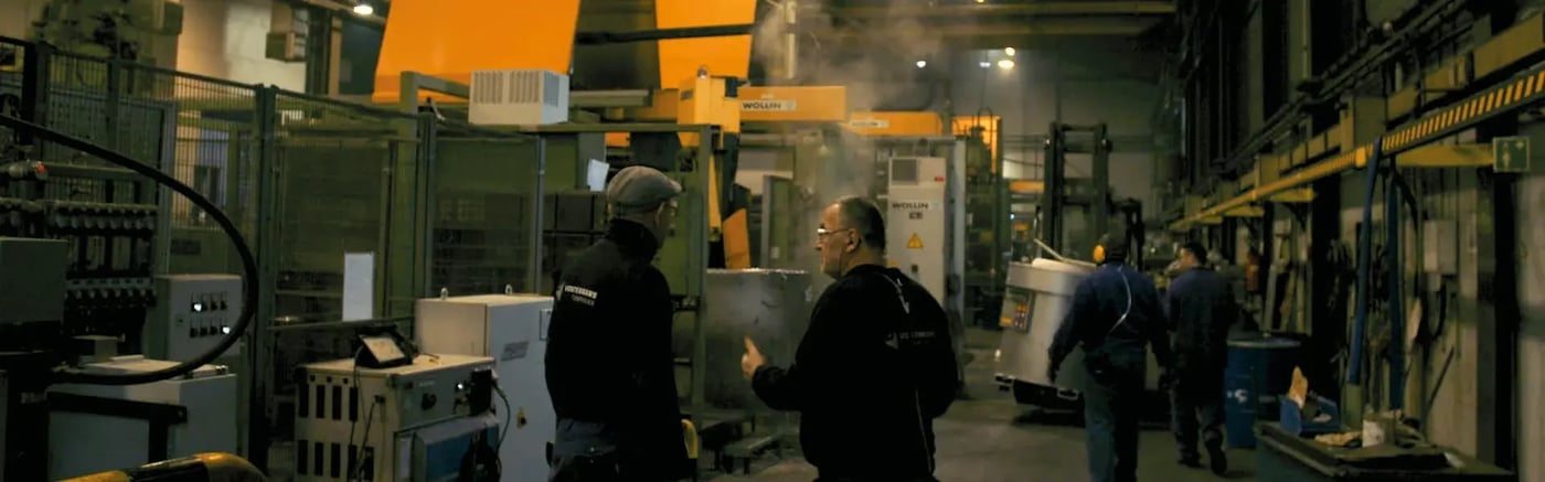 Workers discussing machinery in a high pressure die casting facility with equipment in the background