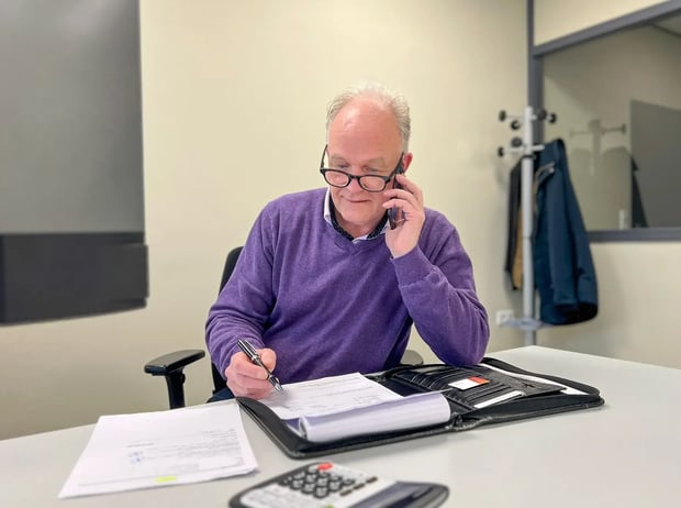 Sales employee in an office talking on the phone while writing notes at a desk
