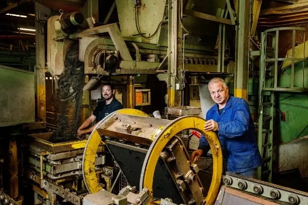 Werknemers bedienen zandgietapparatuur in een industriële omgeving