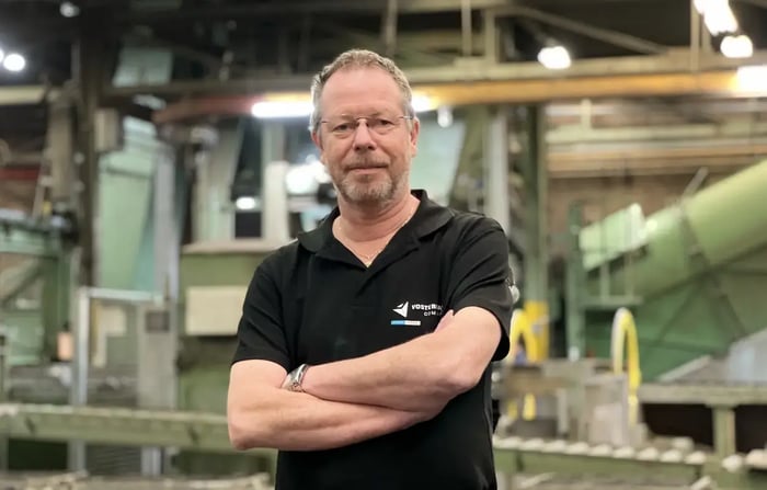 Employee standing with folded arms in front of sand casting machinery in a factory