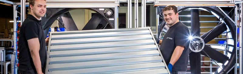 Employés assemblant un grand composant métallique avec un ventilateur industriel en arrière-plan