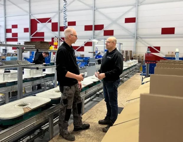 Zwei Männer diskutieren in einer Fabrik in der Nähe eines Förderbands mit Ausrüstungsteilen