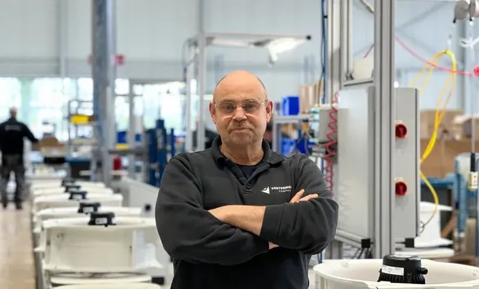 Mann steht in einer Fabrikhalle mit verschränkten Armen vor Maschinen