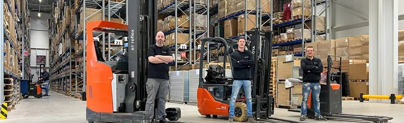 Magazijnmedewerkers staan met vorkheftrucks in een opslaggang omringd door gestapelde rekken