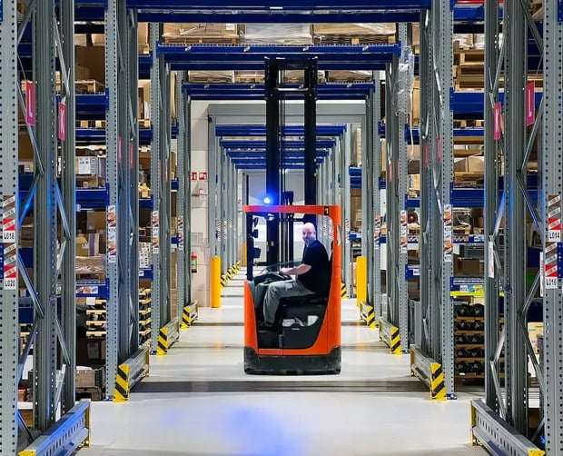 Magazijnmedewerker rijdt met een vorkheftruck door een opslaggang met aan beide zijden rekken