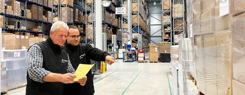 Twee magazijnmedewerkers bespreken en controleren een pallet in een opslaggang