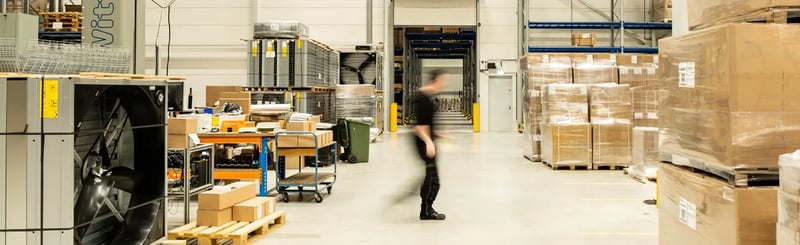 Opslaggang met pallets, dozen en een snel bewegende werknemer op de achtergrond