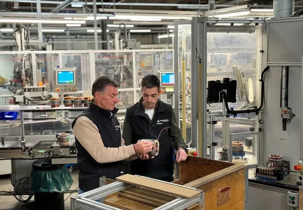 Zwei Arbeiter in einer Fabrik, die Motorenteile prüfen.