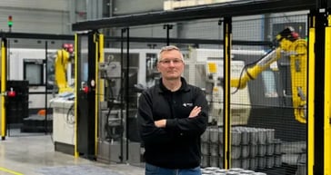 Werknemer staat voor productiemachines met robotarm in fabriek