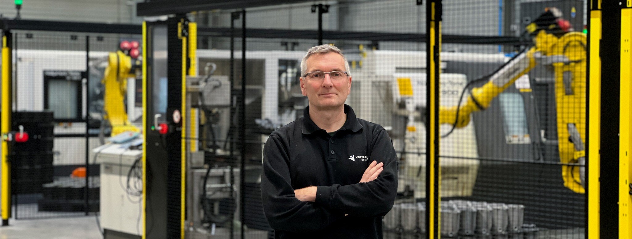 Werknemer staat voor productielijn in fabriek met gele robotarm