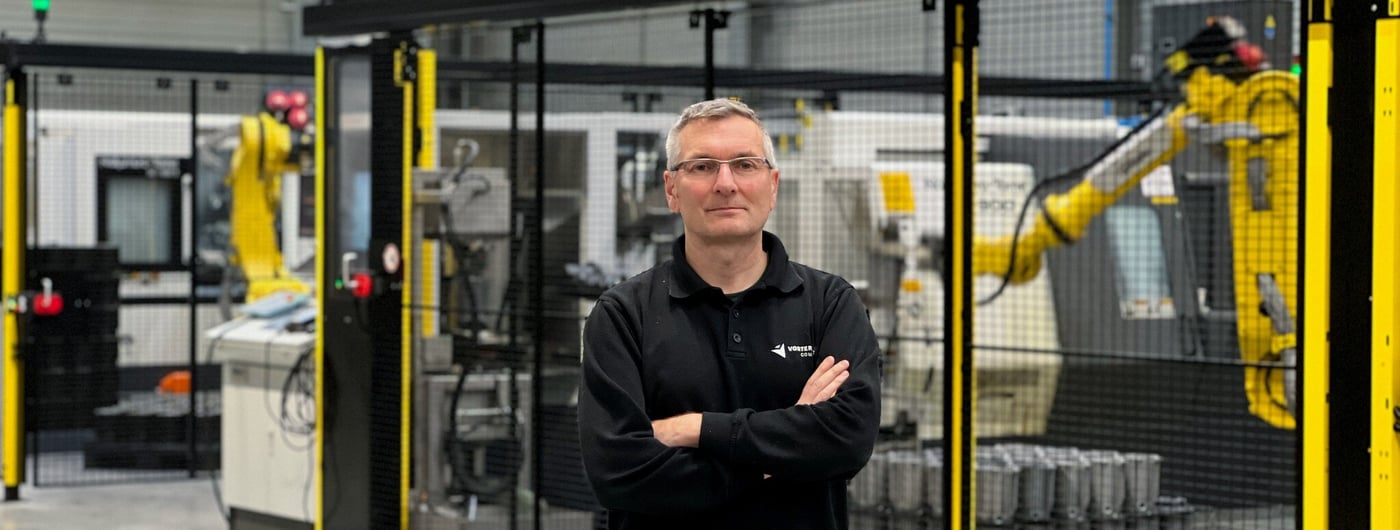 Employee standing in front of factory production line with yellow robotic arm