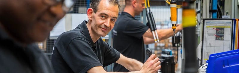 Employé travaillant sur la ligne d'assemblage de moteurs souriant à la caméra avec collègues en arrière-plan
