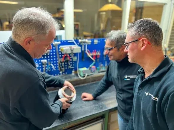 Tres empleados discutiendo componente de motor en un taller