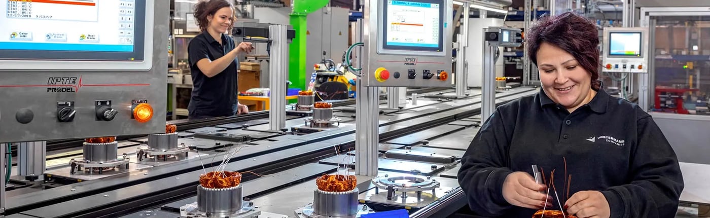 Twee vrouwen werken in een fabriek aan machines die spoelen wikkelen voor ventilatieapparatuur