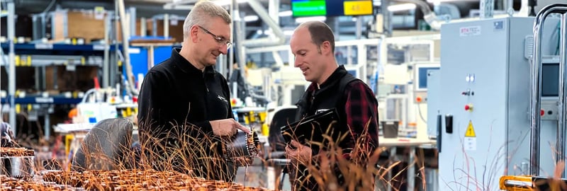 Twee mannen bespreken koperen spoelen in een fabriek met veel spoelen op een tafel