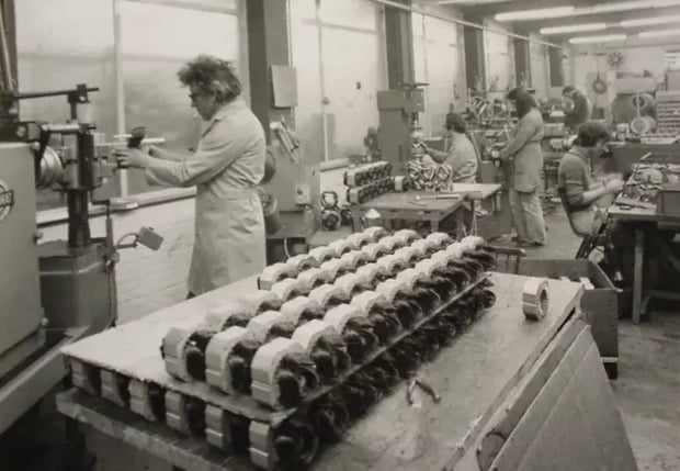 Trabajadores en una fábrica ensamblando motores eléctricos en blanco y negro