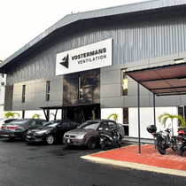 Área de estacionamiento con coches y motos frente a un edificio industrial