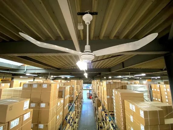 Large ceiling fan in a warehouse with rows of stacked boxes