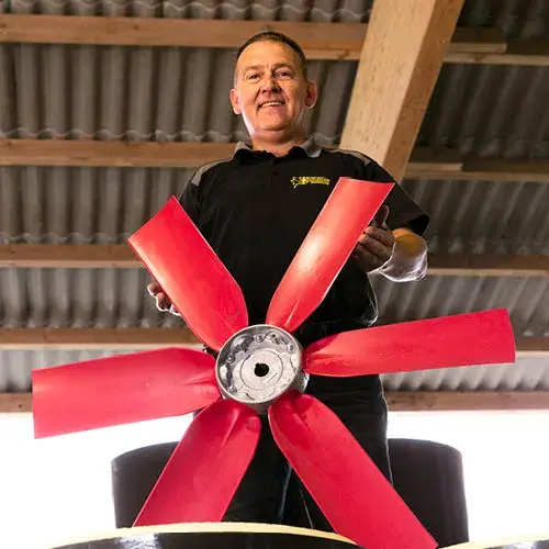 Hombre sonriendo y sosteniendo un gran aspa de ventilador industrial rojo